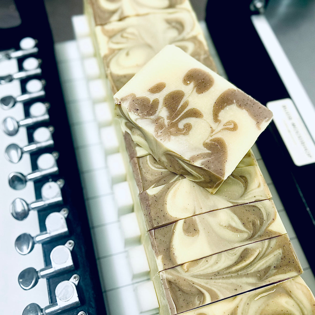 A close-up of artisanal soap bars with a cream and light brown marble swirl pattern, arranged on a white surface next to a black metal soap dispenser.