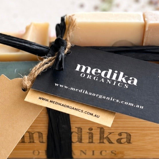 Medika Organics handmade soap bars tied with twine and a branded black paper tag, displayed on a wooden box.