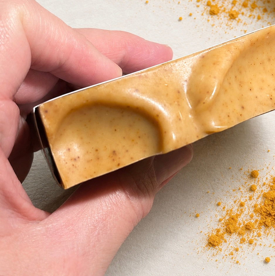 A hand holding a turmeric soap bar