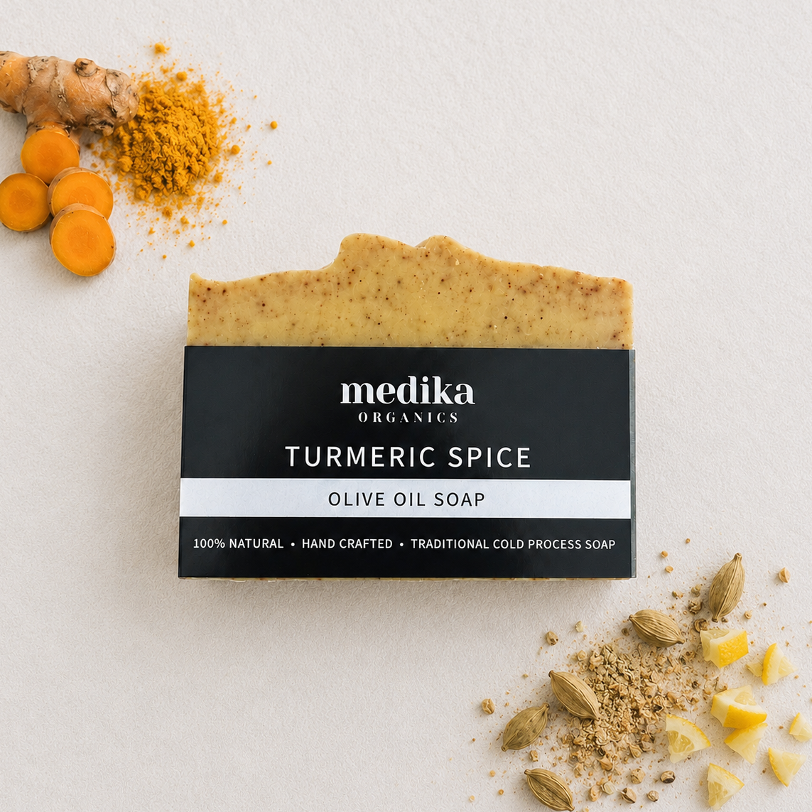 A bar of Medika Organics Turmeric Spice Olive Oil Soap is displayed on a textured off-white background, styled with fresh turmeric root, turmeric powder, and whole spices.