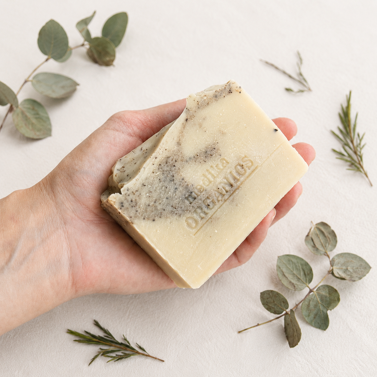 A handmade natural tea tree and eucalyptus soap held in the hand to show its generous size, artisan finish and creamy cold process texture.